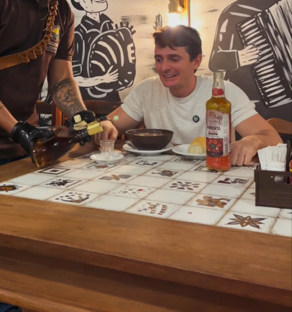 Mesa de madeira com tampo de azulejos, caldinho na cumbuca e garrafa de pimenta artesanal